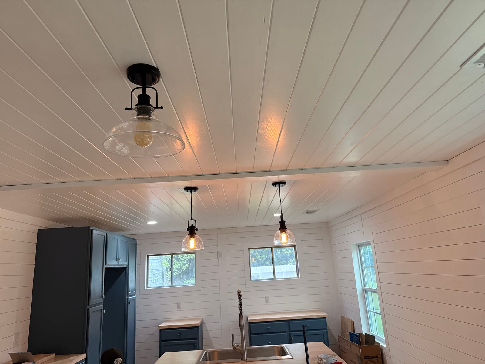 Pendant and recessed lighting fitted to a white board ceiling above a kitchen